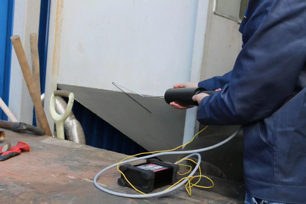 Inspeksi kontinuitas coating menggunakan holiday detector pada permukaan logam